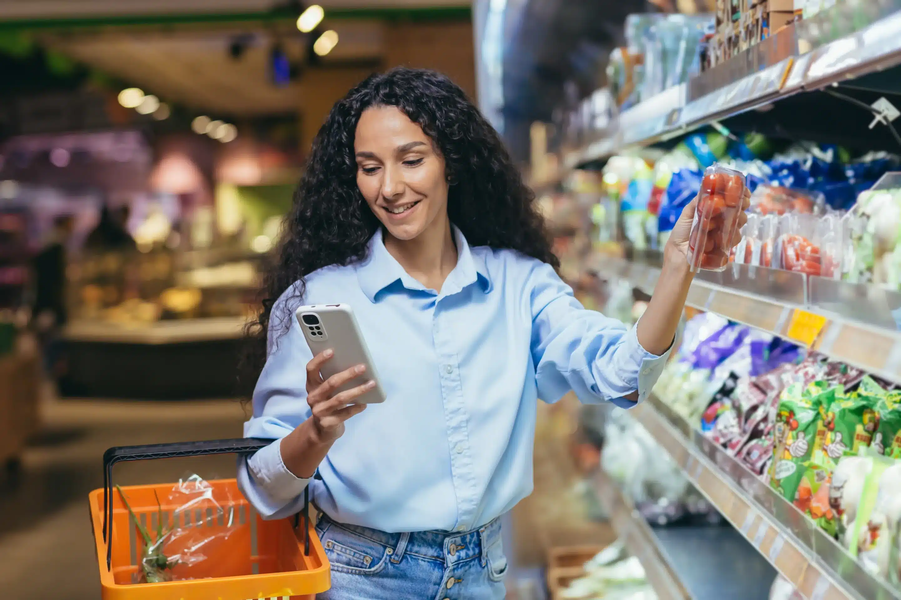 Woman picking out tomatoes in a grocery isle while looking at her grocery list on her phone